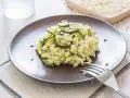 Kremowe risotto z cukinią i orzeszkami pinii, podane na brązowym talerzu.