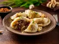 Talerz pełen pysznych pierogów z kapustą i grzybami, posypanych szczypiorkiem. Obok czosnek i pieprz.