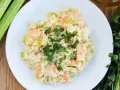 Pyszne risotto z krewetkami, udekorowane natką pietruszki, obok łodygi selera i oliwy.