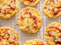 Mini pizze z serka wiejskiego, z kukurydzą i kawałkami mięsa, ułożone na metalowej kratce.