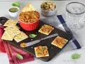 Pyszna pasta z suszonych pomidorów na krakersach, gotowa do degustacji. Obok miseczka z orzechami i szklanka wody.