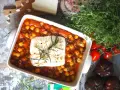 Pyszny gulasz z ciecierzycy w sosie pomidorowym, zapieczony z serem feta i gałązką rozmarynu. Obok świeże pomidory i zioła.