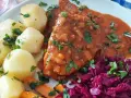 Pyszna szynka w sosie własnym, podana z ziemniakami, marchewką i czerwoną kapustą. Danie posypane jest świeżą natką pietruszki.