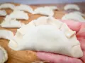 Surowe pierogi na desce, jeden w dłoni. Zastanawiasz się, ile gotować pierogi, by były idealne?