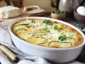 Pyszna zapiekanka z cukinii, udekorowana natką pietruszki i startym parmezanem, prezentuje się apetycznie w białej naczyniu.