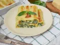 Pyszne cannelloni ze szpinakiem, zapieczone pod beszamelem i serem, podane na talerzu z listkiem bazylii.