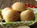 Świeżo upieczone bułki do burgerów, posypane sezamem, czekają w koszyku. Obok gałązka pomidorków koktajlowych.