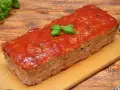 Pyszna pieczeń z mięsa mielonego, polana sosem pomidorowym i ozdobiona listkami bazylii, prezentuje się apetycznie na desce.