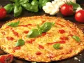 Pyszne ciasto na pizzę z serem, pomidorami i bazylią. Obok leżą świeże pomidory i kalafior.