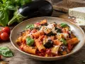 Pyszne pasta alla norma z bakłażanem, pomidorami i bazylią, posypane parmezanem. Obok świeże składniki: bakłażan, pomidorki i ser.