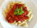 Fusilli z bogatym, domowym makaronem z sosem pomidorowym, udekorowane świeżymi listkami.