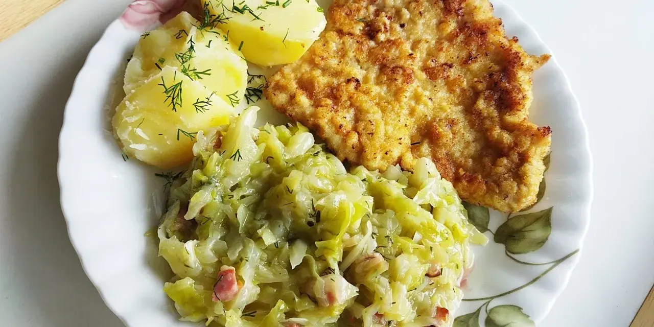 Pyszna kapusta zasmażana z boczkiem, podana z ziemniakami i kotletem.