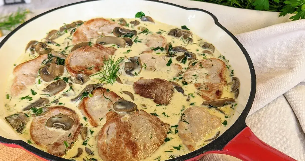 Soczyste polędwiczki w kremowym sosie z pieczarkami i koperkiem, podane w czerwonej patelni. Pyszne danie gotowe do podania.