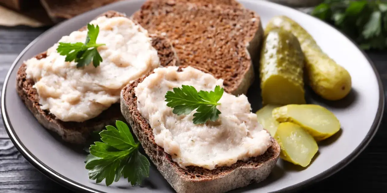Domowy smalec przepis babci na ciemnym chlebie, ozdobiony natką pietruszki, z ogórkami kiszonymi. Pyszne, tradycyjne danie.