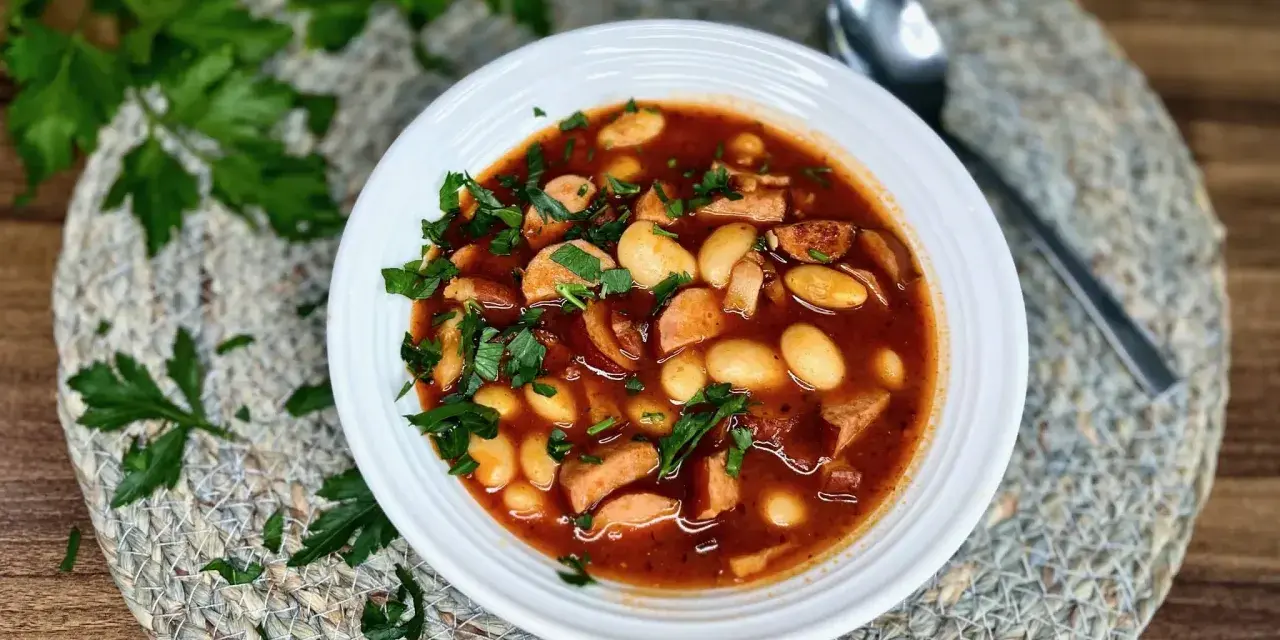 Aromaticzna fasolka po bretońsku z kiełbasą i fasolą, posypana świeżą natką pietruszki, czeka na talerzu.