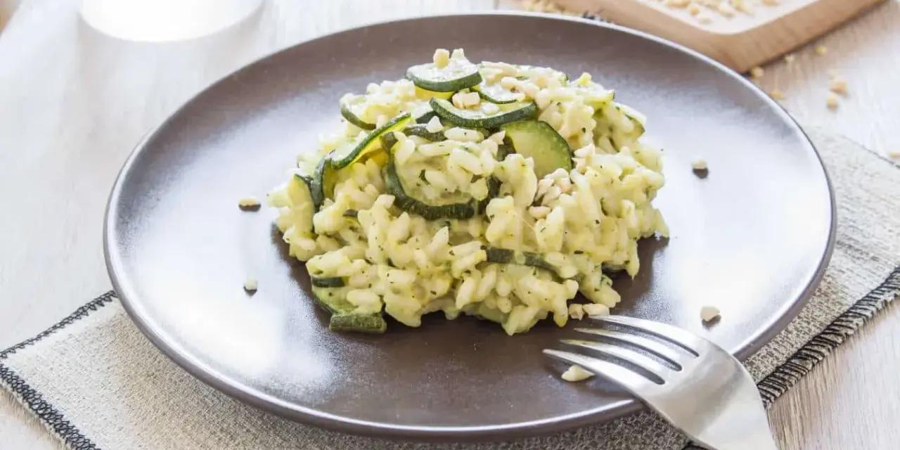 Kremowe risotto z cukinią i orzeszkami pinii, podane na brązowym talerzu.