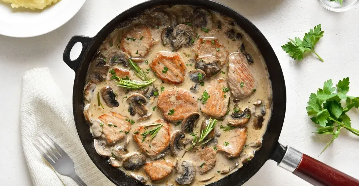 Pyszne polędwiczki w sosie pieczarkowym, podane w patelni, z gałązkami rozmarynu i posypane natką pietruszki. Obok puree ziemniaczane.