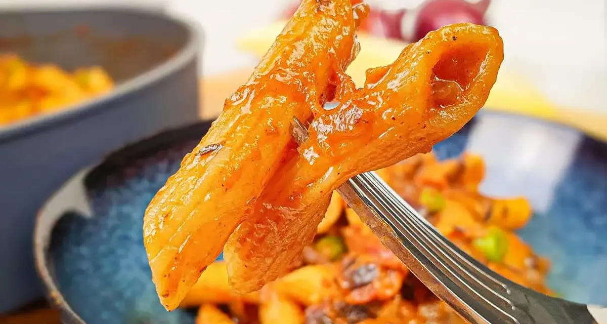 Widok z bliska na widelcu, na którym znajduje się makaron penne z sosem pomidorowym i kawałkami chorizo.