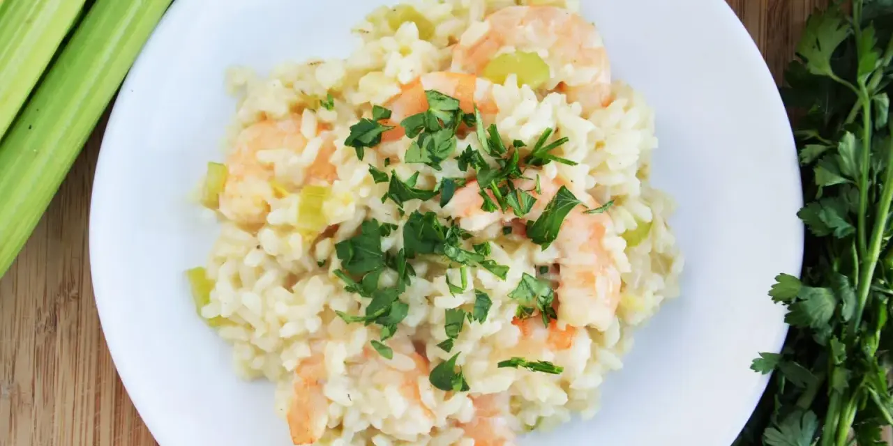 Pyszne risotto z krewetkami, udekorowane natką pietruszki, obok łodygi selera i oliwy.