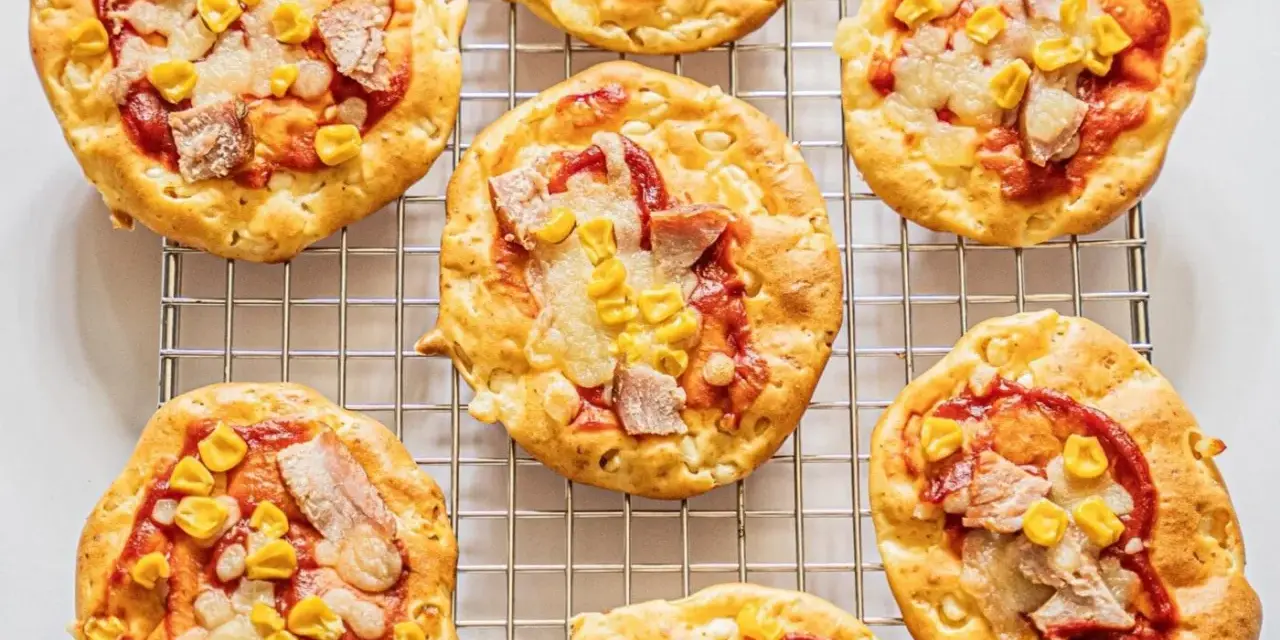 Mini pizze z serka wiejskiego, z kukurydzą i kawałkami mięsa, ułożone na metalowej kratce.