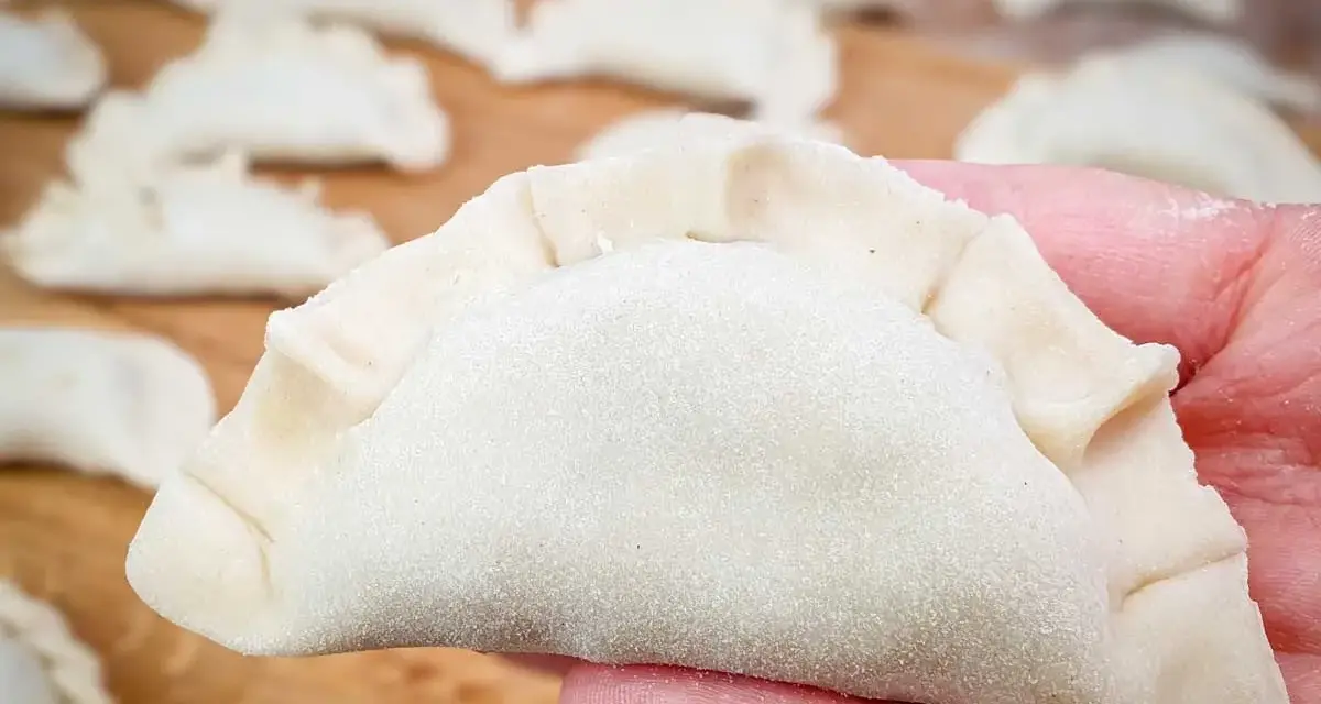 Surowe pierogi na desce, jeden w dłoni. Zastanawiasz się, ile gotować pierogi, by były idealne?