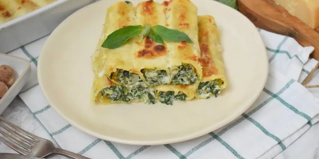 Pyszne cannelloni ze szpinakiem, zapieczone pod beszamelem i serem, podane na talerzu z listkiem bazylii.