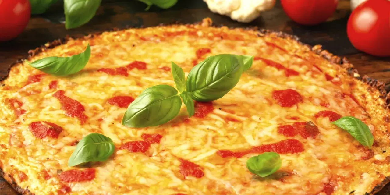 Pyszne ciasto na pizzę z serem, pomidorami i bazylią. Obok leżą świeże pomidory i kalafior.