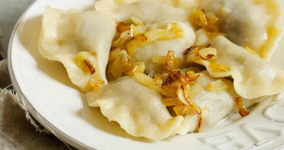 Pyszne pierogi z mięsem, polane skwarkami z cebulki, na białym talerzu.