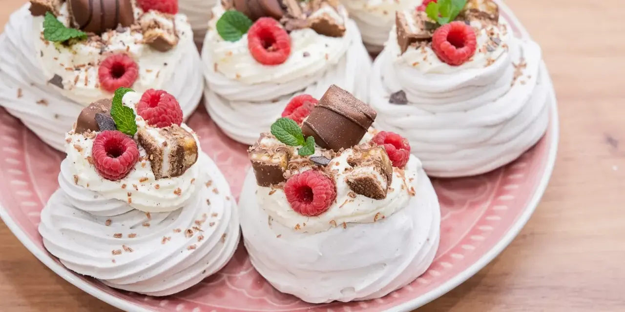 Mini bezy Pavlova z malinami i czekoladą, udekorowane listkami mięty. Idealne na deser.