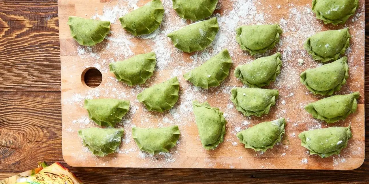 Zielone pierogi ze szpinakiem ułożone na desce, posypane mąką. Czekają na gotowanie.