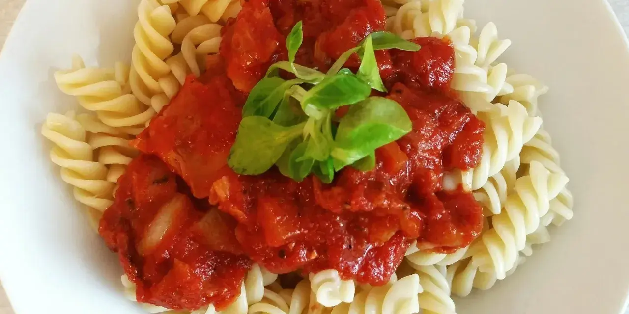 Fusilli z bogatym, domowym makaronem z sosem pomidorowym, udekorowane świeżymi listkami.