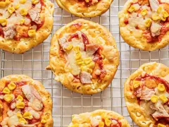 Mini pizze z serka wiejskiego, z kukurydzą i kawałkami mięsa, ułożone na metalowej kratce.