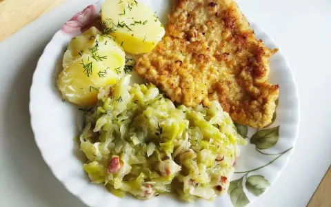 Pyszna kapusta zasmażana z boczkiem, podana z ziemniakami i kotletem.