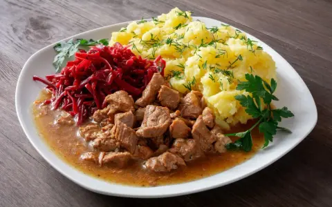 Pyszny gulasz z łopatki w sosie, podany z purée ziemniaczanym i surówką z buraczków.