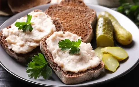 Domowy smalec przepis babci na ciemnym chlebie, ozdobiony natką pietruszki, z ogórkami kiszonymi. Pyszne, tradycyjne danie.