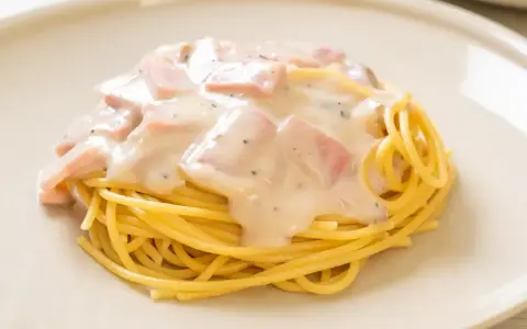 Pyszny makaron z serem i kawałkami szynki, polany kremowym sosem. Idealny na szybki obiad.