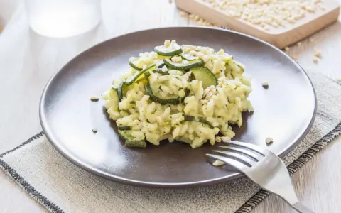 Kremowe risotto z cukinią i orzeszkami pinii, podane na brązowym talerzu.