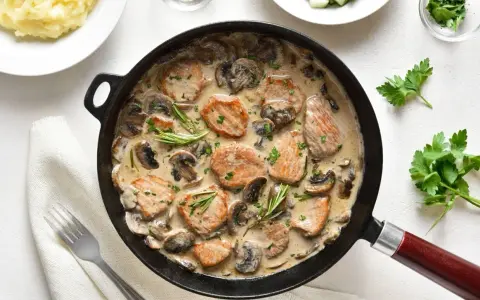 Pyszne polędwiczki w sosie pieczarkowym, podane w patelni, z gałązkami rozmarynu i posypane natką pietruszki. Obok puree ziemniaczane.