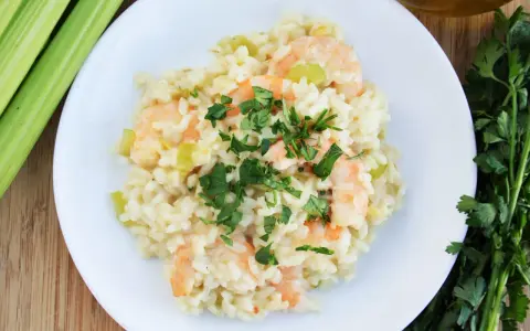 Pyszne risotto z krewetkami, udekorowane natką pietruszki, obok łodygi selera i oliwy.