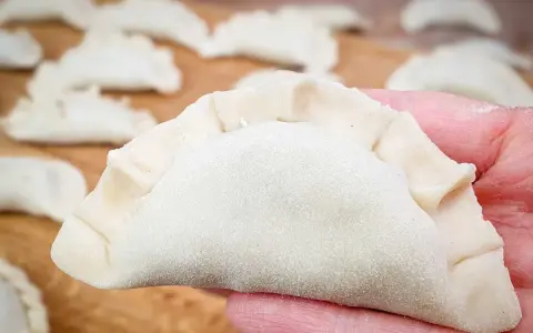 Surowe pierogi na desce, jeden w dłoni. Zastanawiasz się, ile gotować pierogi, by były idealne?