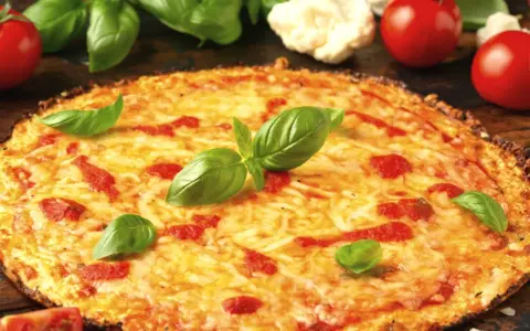 Pyszne ciasto na pizzę z serem, pomidorami i bazylią. Obok leżą świeże pomidory i kalafior.
