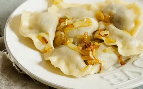Pyszne pierogi z mięsem, polane skwarkami z cebulki, na białym talerzu.