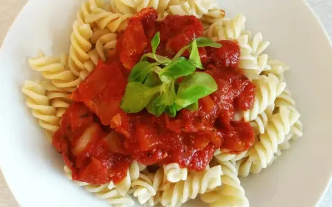 Fusilli z bogatym, domowym makaronem z sosem pomidorowym, udekorowane świeżymi listkami.