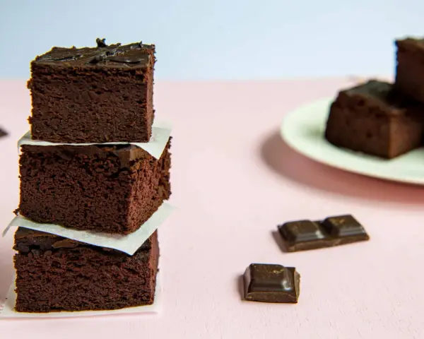 Ciemne, wilgotne brownie z fasoli, ułożone w wieżę, obok kawałków czekolady.