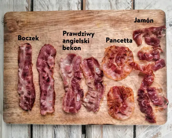 Boczek, prawdziwy angielski bekon, pancetta i jamón ułożone na desce. Różne rodzaje wędlin, każdy z nich ma swój unikalny wygląd.