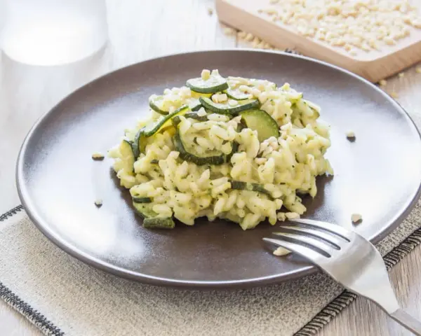 Kremowe risotto z cukinią i orzeszkami pinii, podane na brązowym talerzu.