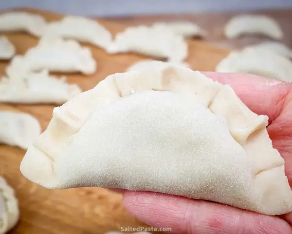 Surowe pierogi na desce, jeden w dłoni. Zastanawiasz się, ile gotować pierogi, by były idealne?