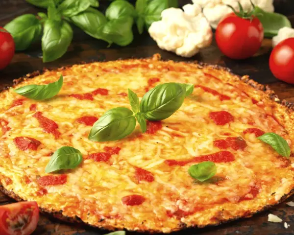 Pyszne ciasto na pizzę z serem, pomidorami i bazylią. Obok leżą świeże pomidory i kalafior.
