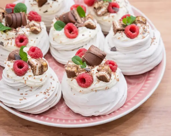 Mini bezy Pavlova z malinami i czekoladą, udekorowane listkami mięty. Idealne na deser.