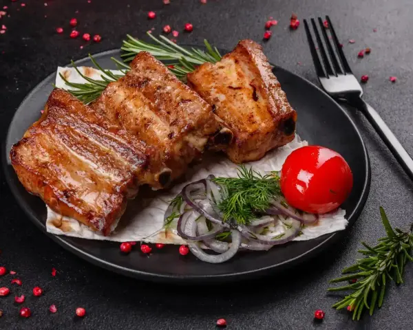 Soczyste, pieczone żeberka w rękawie, podane z pomidorkiem, cebulą i rozmarynem.